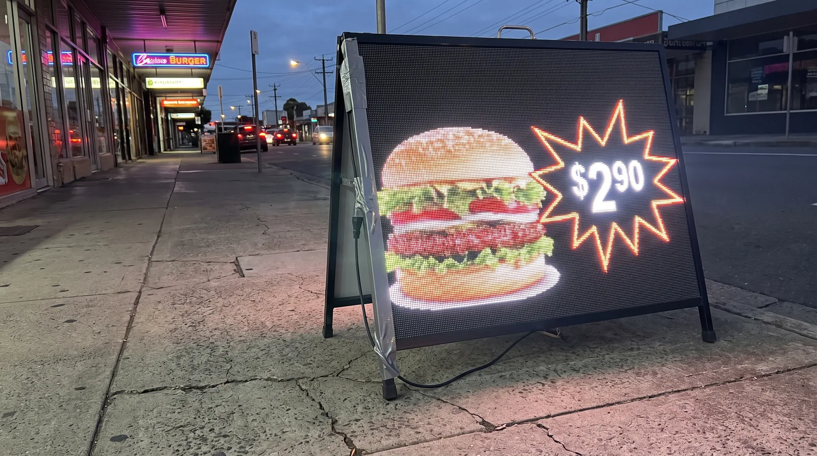 Digital A-frame signage glowing outside a burger shop at dusk